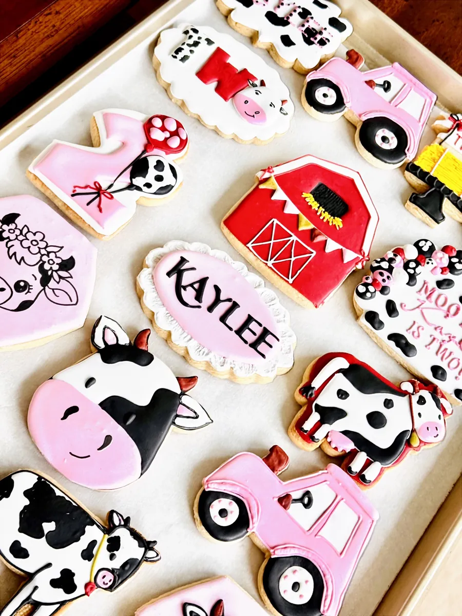 Pink cow and farm themed second birthday cookies with tractor, red barn, cow faces and personalized name plaque